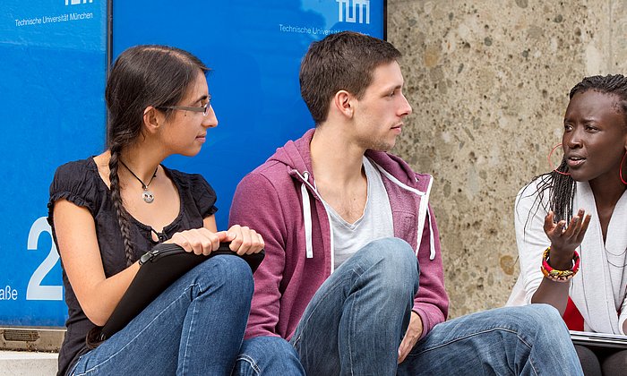 Studierende sitzen auf der Treppe des Haupteingangs der TUM.