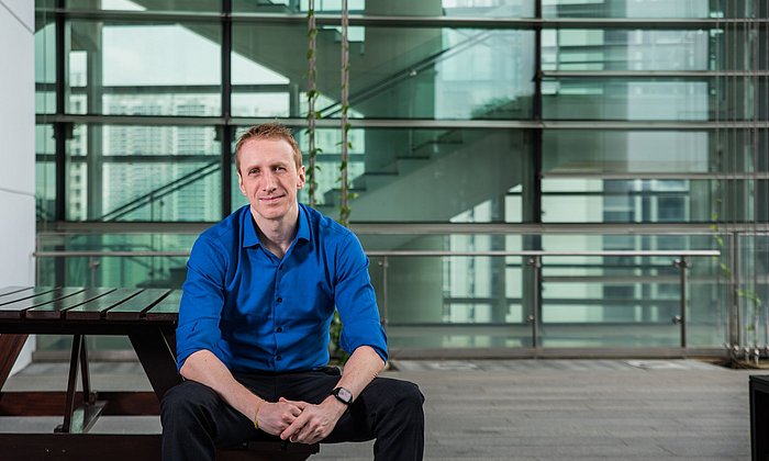 Scientist at the Singapore campus Dr. David Eckhoff, sitting in front of a glass building.