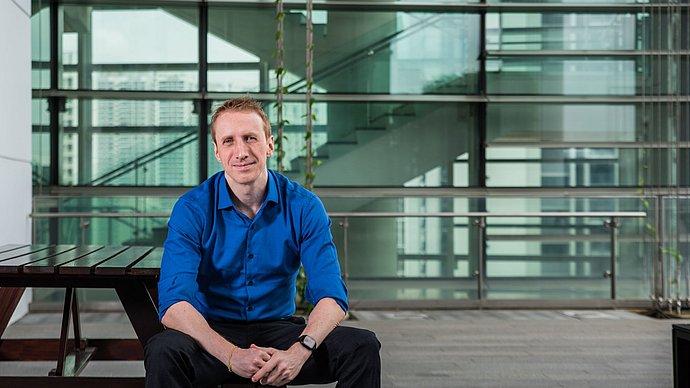 Wissenschaftler am Campus Singapur Dr. David Eckhoff, der vor einem gläsernen Gebäude sitzt.