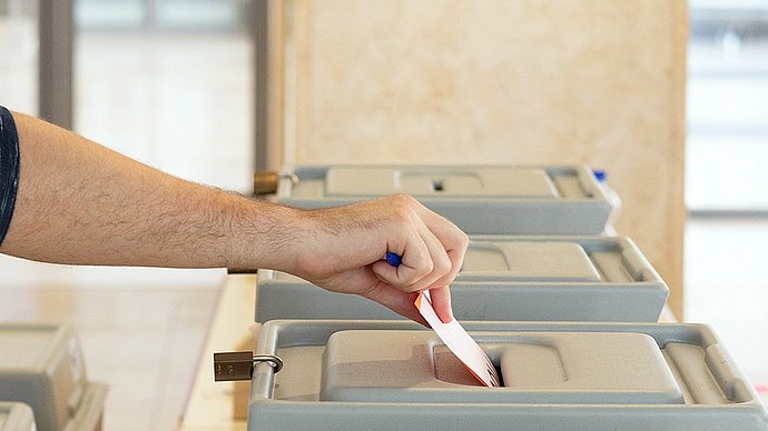 Detail of photograph of a student casting a ballot into a ballot box.