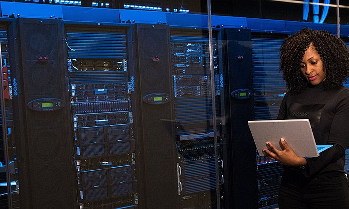 Woman with laptop in front of server racks.