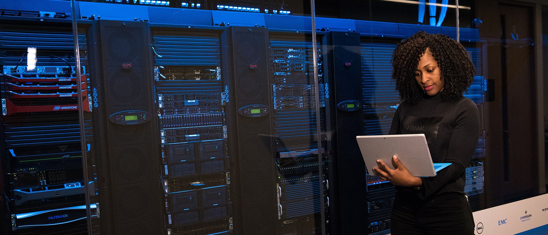 Woman with laptop in front of server racks.