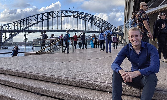 Dokorand Tobias Teschemacher sitzt vor einer Brücke in Brisbane, Australien. 