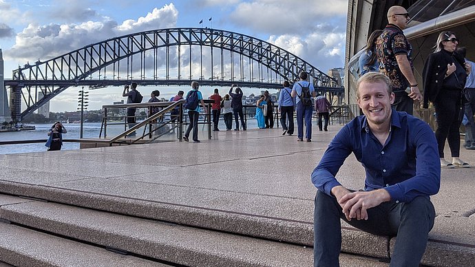 Dokorand Tobias Teschemacher sitzt vor einer Brücke in Brisbane, Australien. 