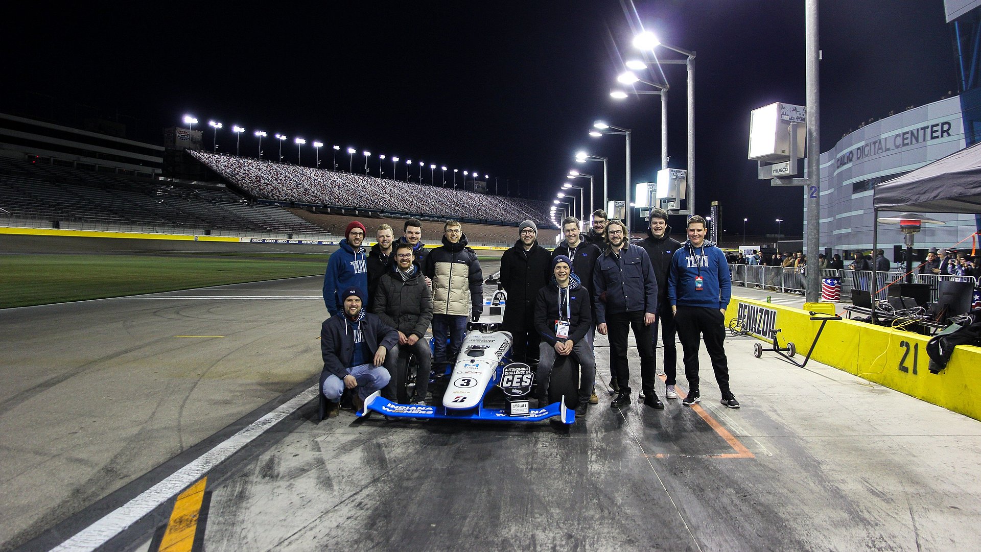 The team together with the winning vehicle. A group of scientists stand around a formula racing car.