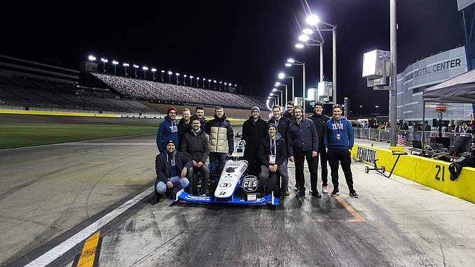 A group of scientists stand around a formula racing car.