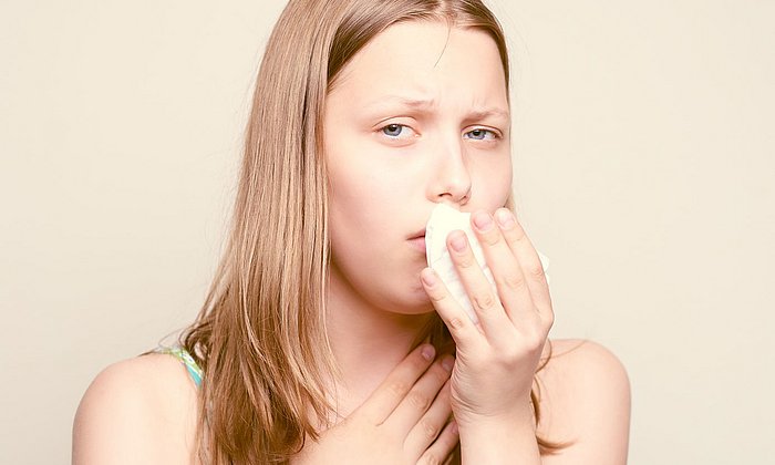 A sick teen girl is coughing in a tissue.