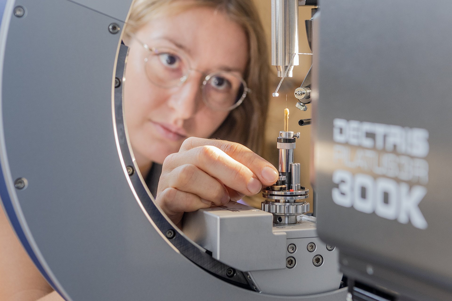 Anna Vogel beim Montieren eines Einkristalls auf dem Einkristalldiffraktometer. Vor ihr ist eine Glaskapillare zu sehen, auf der sich ein Kristall von etwa 0,2 mm Durchmesser befindet. Mit geeigneter Messstrahlung werden Daten aufgenommen, um hieraus die Struktur zu bestimmen.