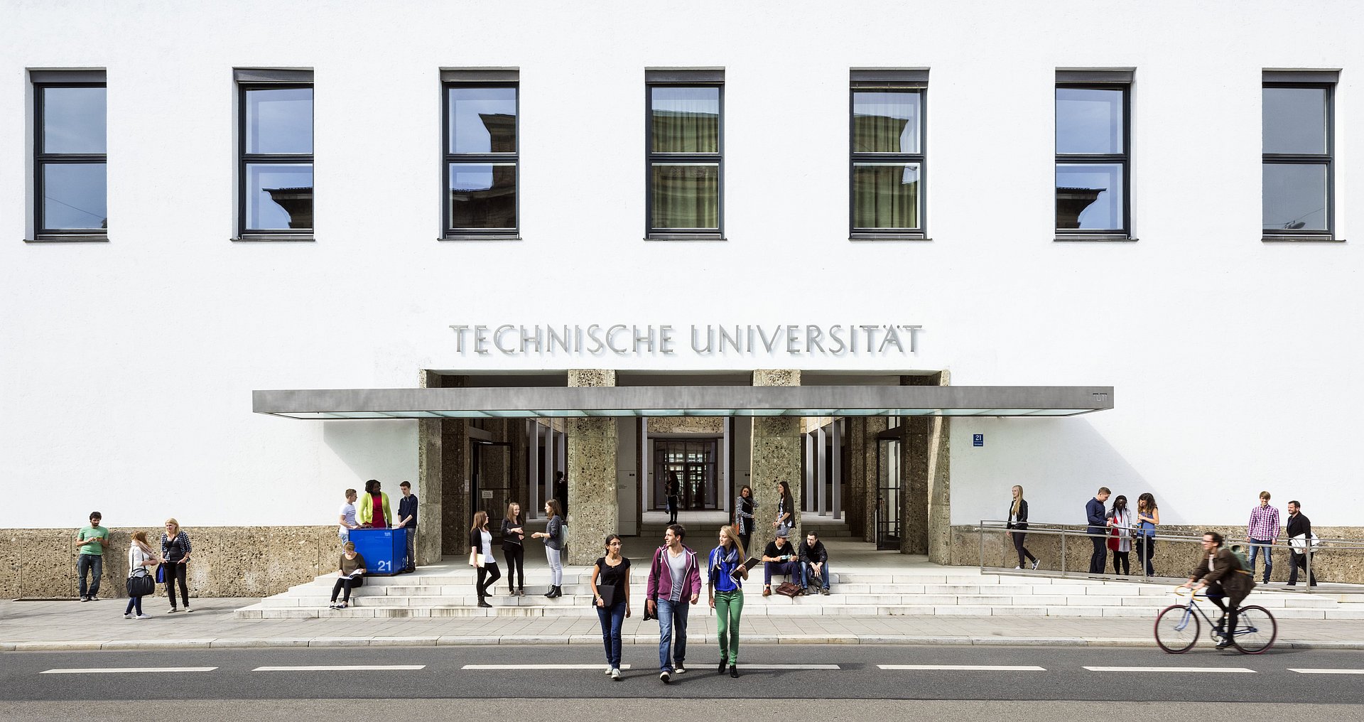 Der Haupteingang der Technischen Universität München am Stammgelände. Einige Studieninteressiere kommen und gehen.