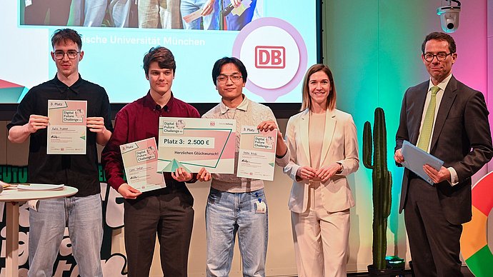 The three students of the “RollsRoICE” team together with two additional individuals on stage at the final of the Digital Future Challenge 2026, presenting their certificates to the audience.