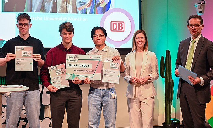 The three students of the “RollsRoICE” team together with two additional individuals on stage at the final of the Digital Future Challenge 2026, presenting their certificates to the audience.