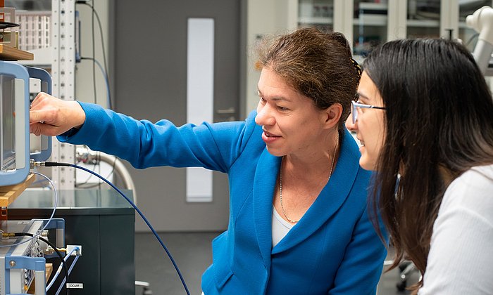 Prof. Weig (links) und ihre Doktorandin Maria Kallergi sitzen vor einem Gerät und diskutieren die Testergebnisse bei der Messung einer Nanosaite. 