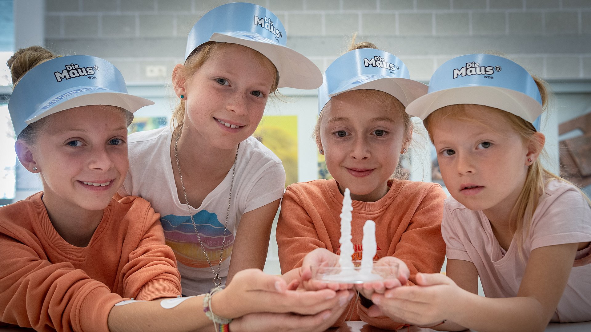 Vier Mädchen mit blaDie-Maus-Kappen halten eine Petrischale in der Hand.