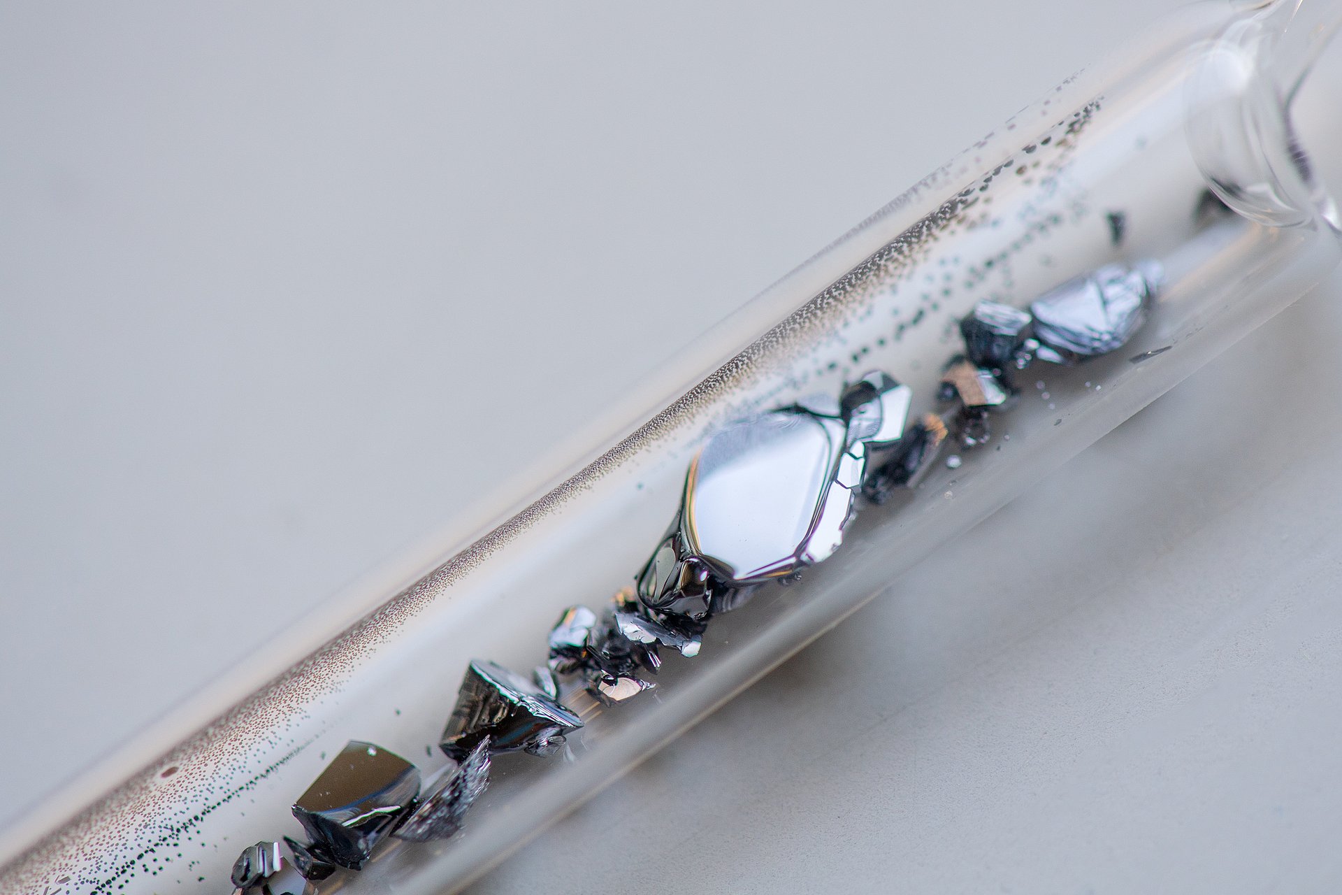Das Bild zeigt große Kristalle von Ag18Cu3Te11Cl3, die sich in einer Silicaglas-Ampulle befinden. In dieser Ampulle wird unter Vakuum die Verbindung aus den Elementen, Silber, Kupfer, Tellur und den Halogeniden hergestellt.