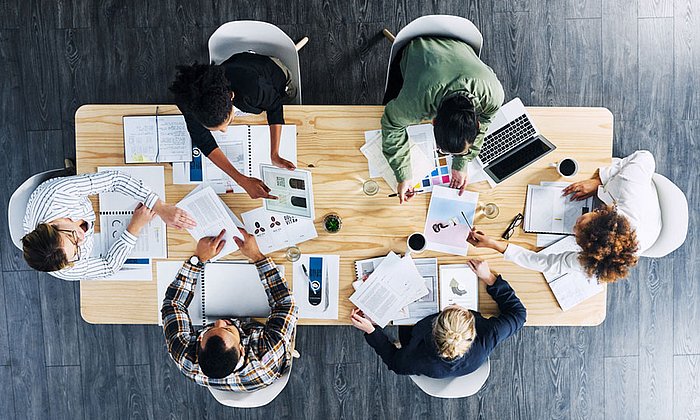 Blick von oben auf eine Gruppe am Bürotisch. (Bild: istockphoto.com / Dean Mitchell)