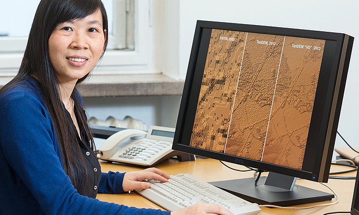 Professor Xiaoxiang Zhu in front of a computer display showing satellite images.