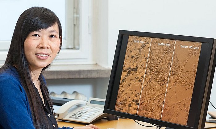 Prof. Xiaoxiang Zhu vor einem Comptuerbildschirm, auf dem Satellitenbilder zu sehen sind.