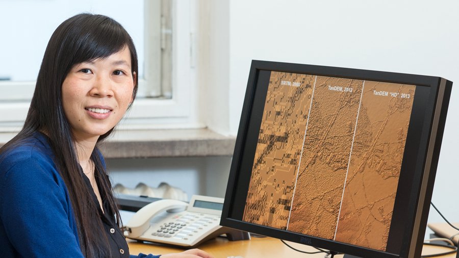Prof. Xiaoxiang Zhu vor einem Comptuerbildschirm, auf dem Satellitenbilder zu sehen sind.