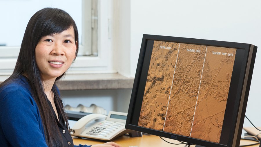 Prof. Xiaoxiang Zhu untersucht in einem neuen ERC-geförderten Projekt das Wachstum von Städten mithilfe einer Kombination von Satelliten-Informationen und Daten von Crowdsourcing-Plattformen. (Bild: U. Benz / TUM) Prof. Xiaoxiang Zhu vor einem Comptuerbildschirm, auf dem Satellitenbilder zu sehen sind.