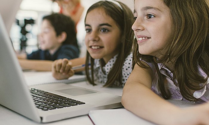 Schülerinnen und Lehrerin an einem Tablet