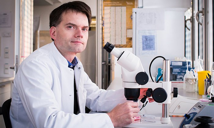 Professor Thomas Korn sitting in front of a microscope .