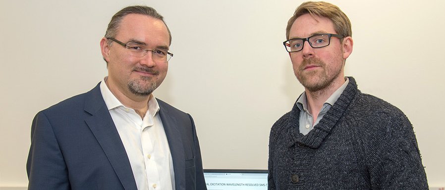 Prof. Dr. Juergen Hauer (li) und Erstautor Erling Thyrhaug mit ihrem Messinstrument. Im Hintergrund Spektren, die damit aufgenommen wurden. (Bild: A. Battenberg / TUM)