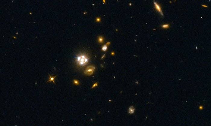 HE0435-1223, in der Mitte des Bildes, gehört zu den fünf besten Gravitationslinsen-Quasaren, die bisher entdeckt wurden. Die Vordergrundgalaxie erzeugt hier vier nahezu gleichmäßig verteilte Bilder des dahinter liegenden Quasars. Bild: Suyu et al. / ESA/Hubble, NASA