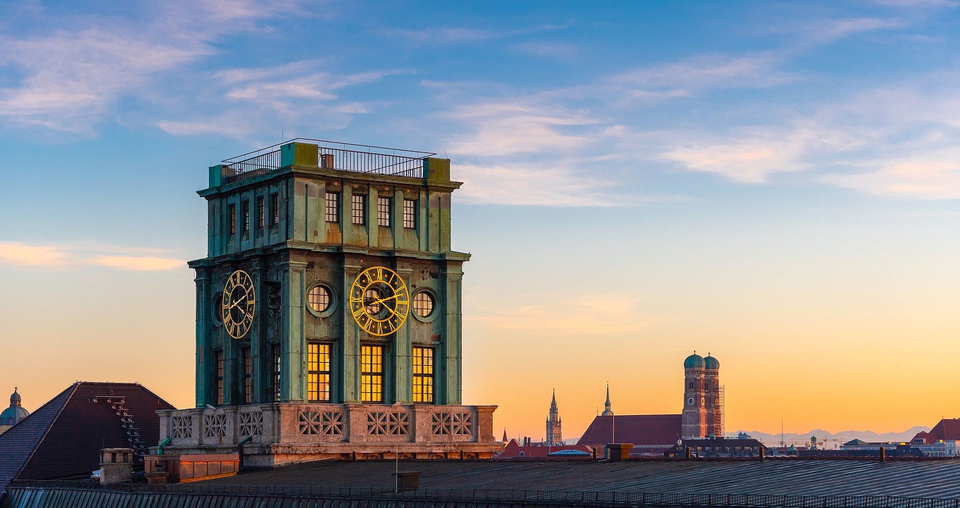 Die Skyline der Münchner Innenstadt bei Sonnenuntergang. Im Fokus steht der Thiersch-Turm, ein Glockenturm und das Wahrzeichen der TUM.