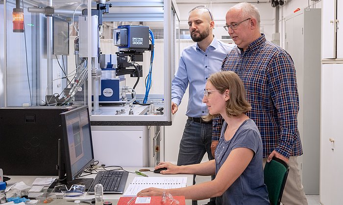 Das Foto zeigt Dr. Venturini (links), Prof. Nilges und Erstautorin Anna Vogel vor einem Messgerät zur Bestimmung von Kristallstrukturen, einem sogenannten Einkristalldiffraktometer.