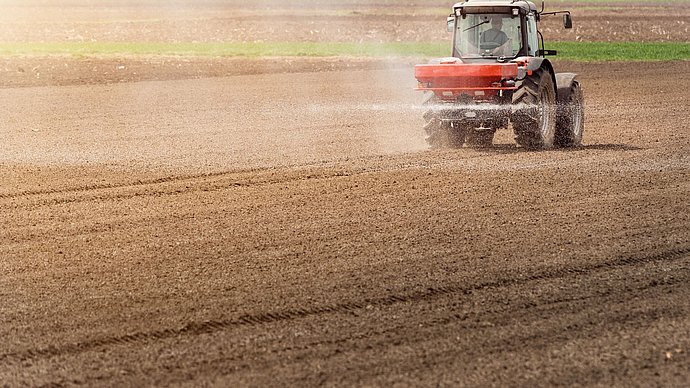 Ein Traktor fährt über einen Acker und trägt im Sprühnebel Stickstoff-Dünger auf.