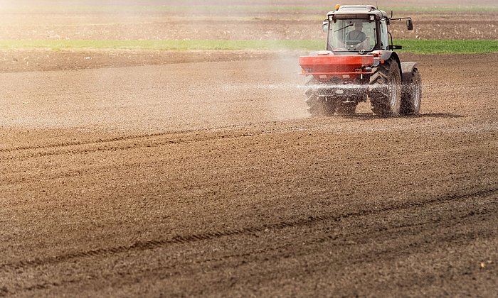 A tractor drives over a field and applies nitrogen fertilizer in a spray mist.