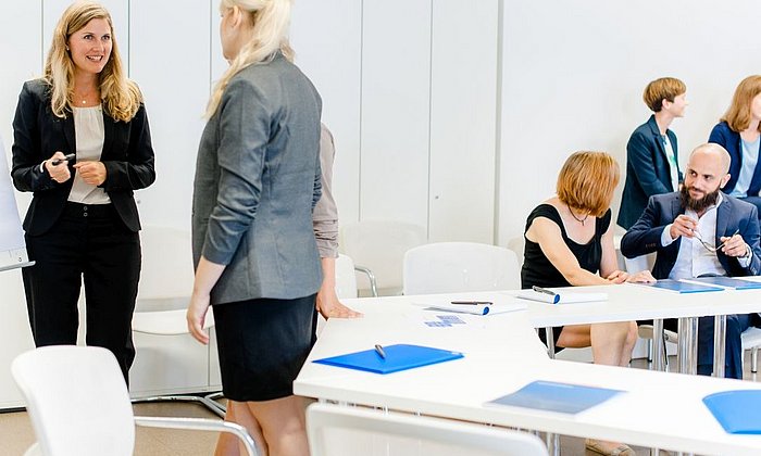 Several women and one man are in a seminar room. They are doing group work in teams of two.