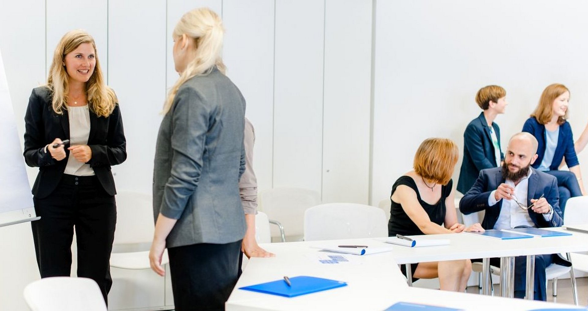 Mehrere Frauen und ein Mann sind in einem Seminarraum. Sie führen eine Gruppenarbeit in jeweils in Zweierteams aus.