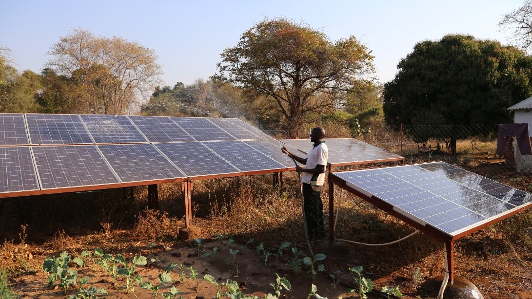 Man is cleaning solar modules of a photovoltaic system with the help of a garden hose, which are part of a TUM project in Zimbabwe.