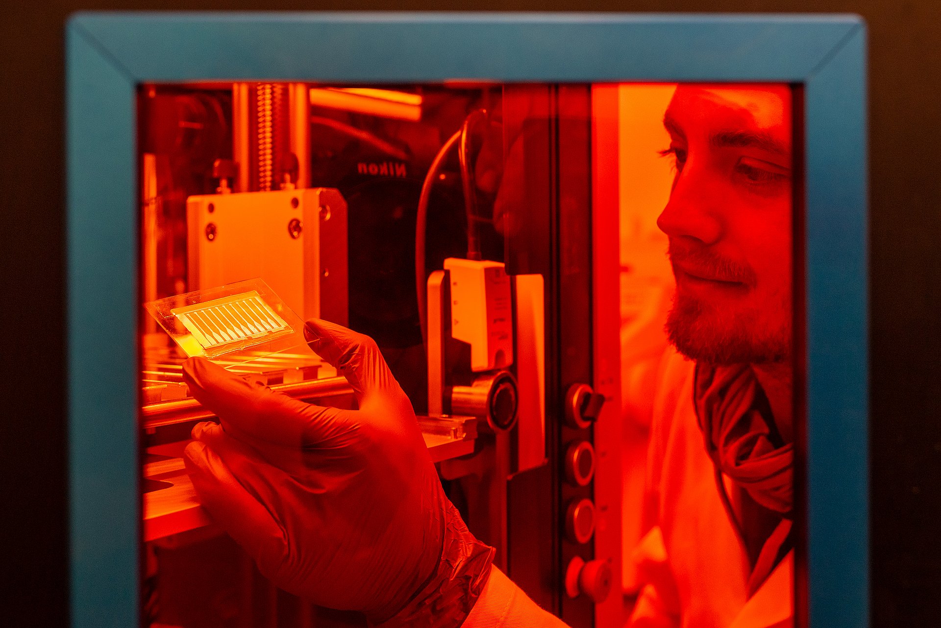 Mit Hilfe von Laserpulsen wird die aufgedampfte Goldschicht in leitfähige Bahnen strukturiert. Lukas Hiendlmeier entnimmt die strukturierten Exemplare aus dem Lasersystem.