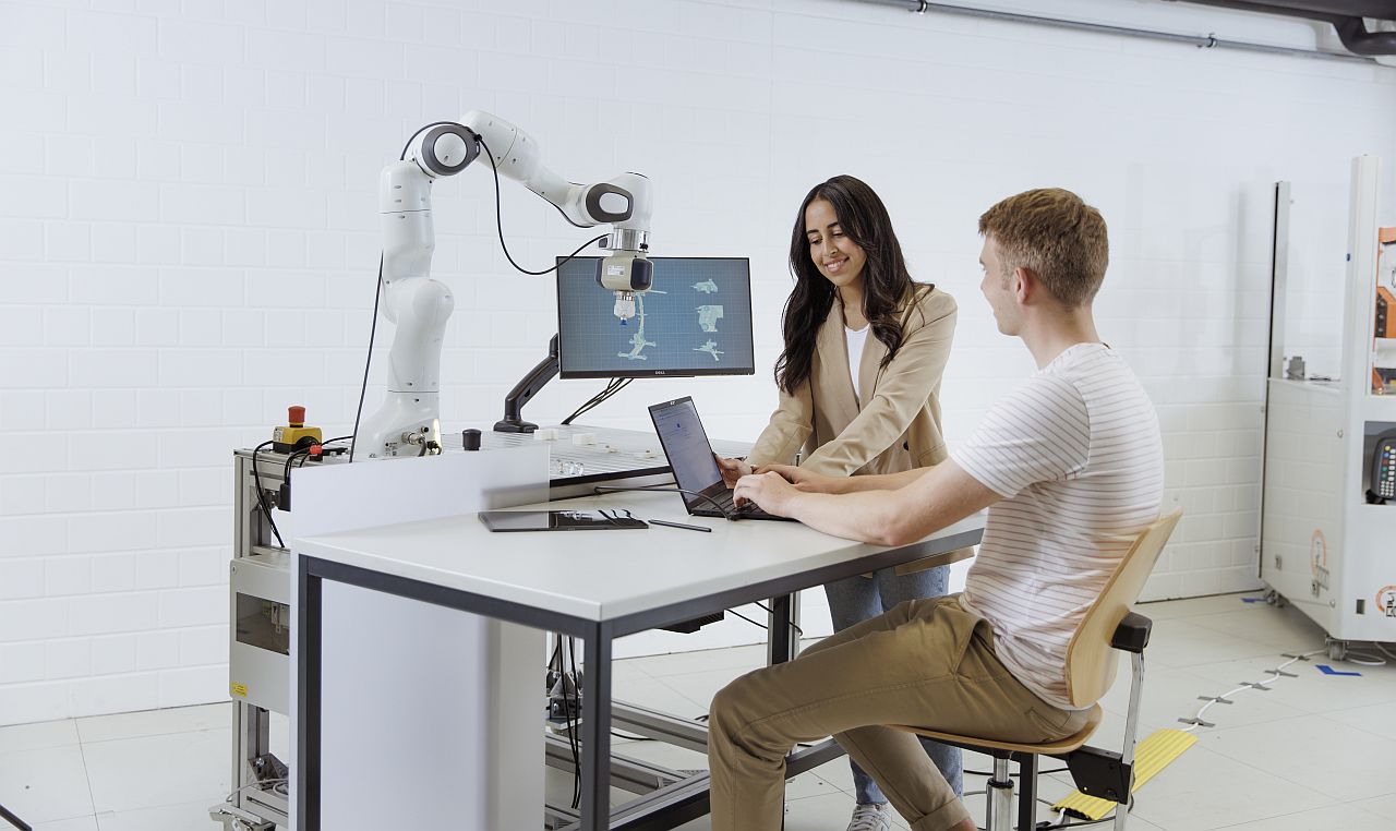 Students work with computers and robotic arms.