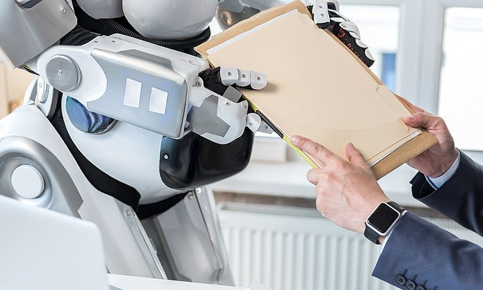A man hands documents to a robot.