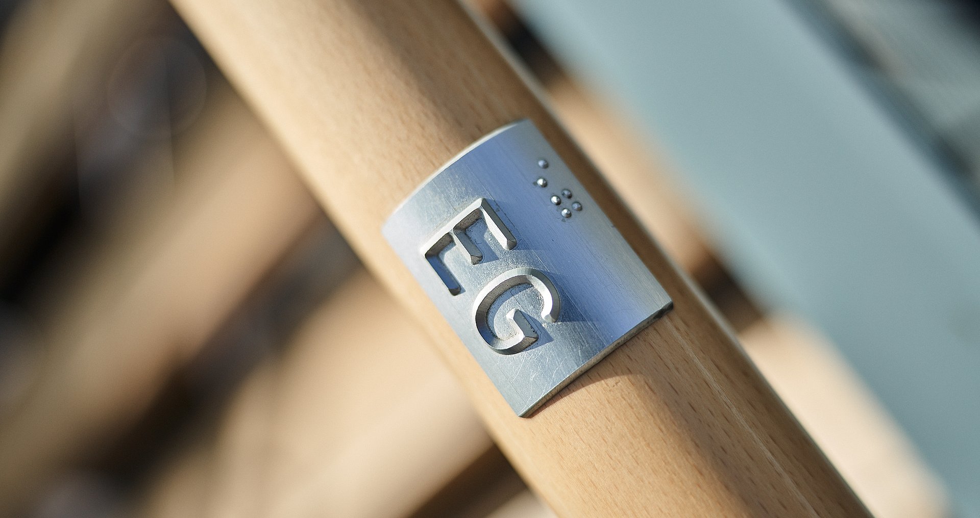 [Translate to English:] Nahaufnahme Holzgeländer mit Plakette auf der EG in Brailleschrift steht.