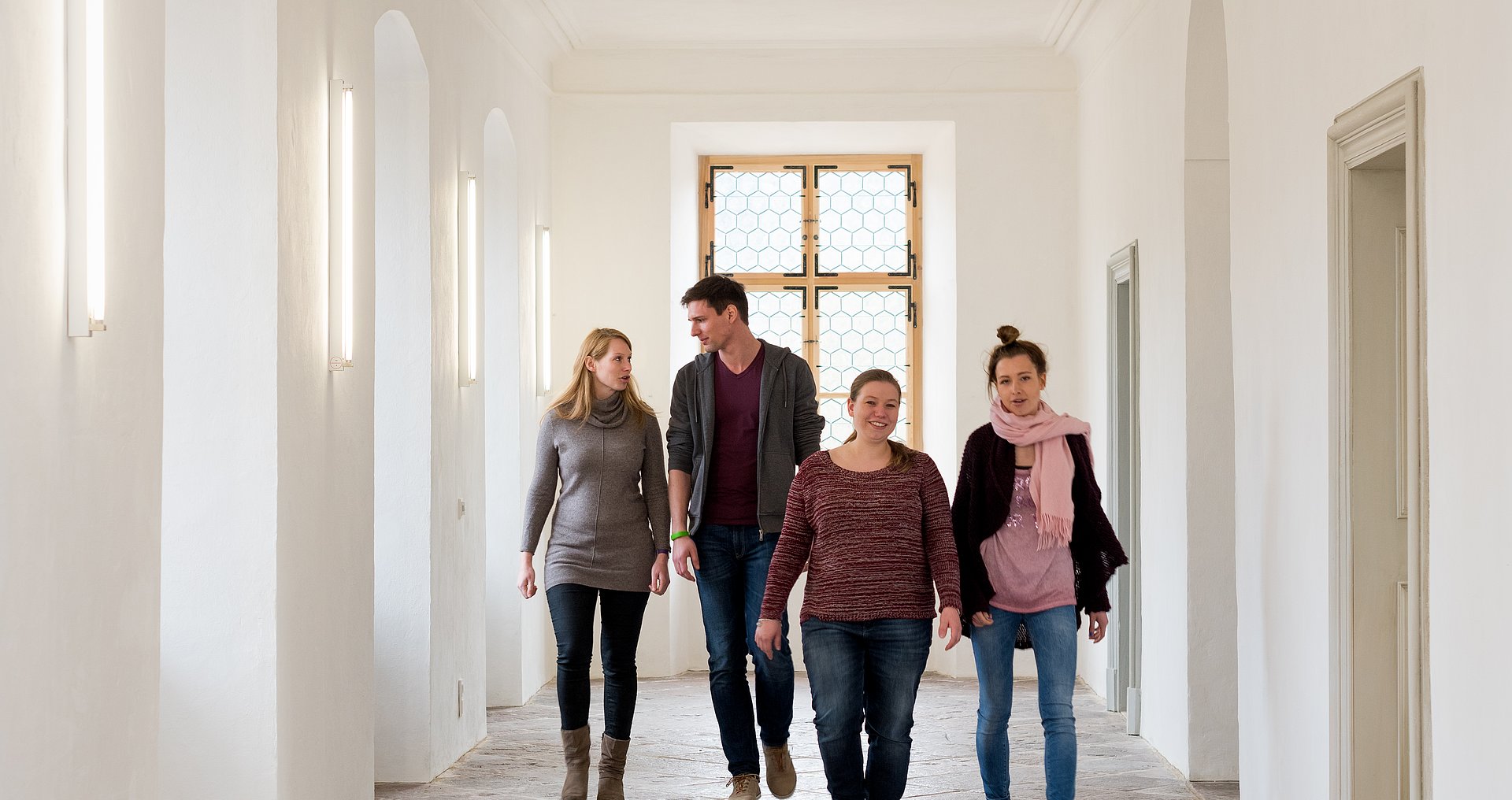 Vier Leute gehen einen Gang am Innenstadtcampus entlang und unterhalten sich dabei.