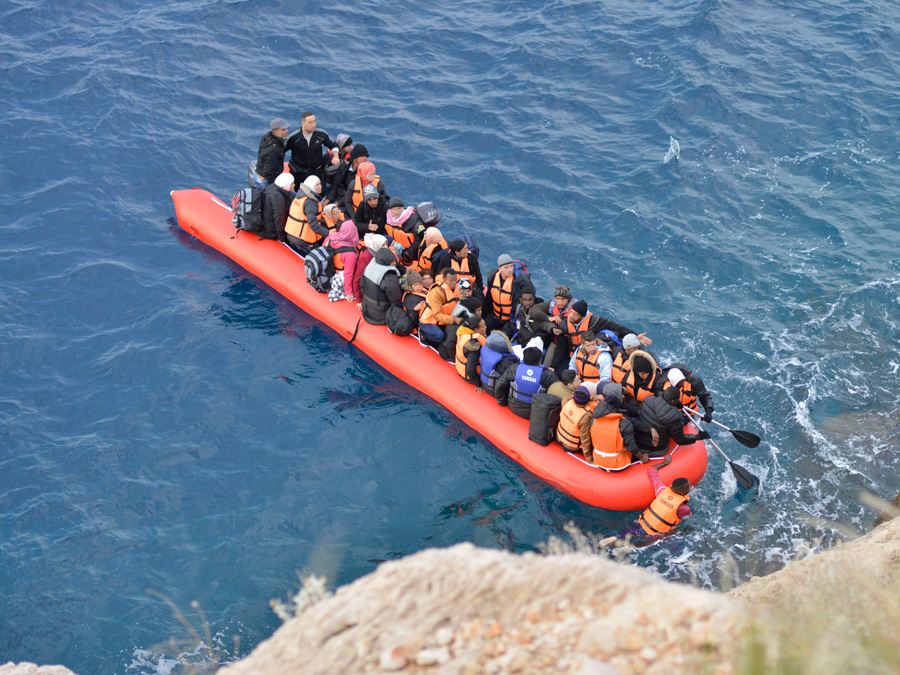 Menschen auf einem Schlauchboot vor einer Steilküste.