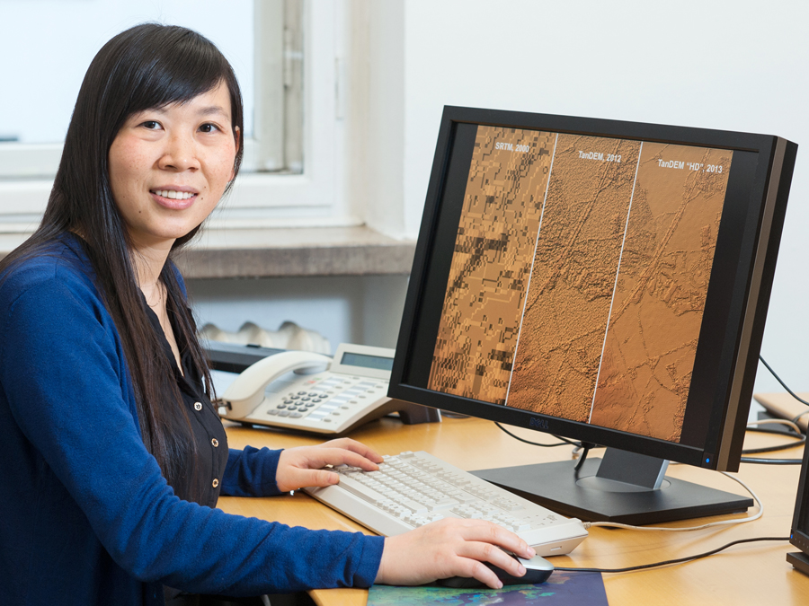 Professor Xiaoxiang Zhu in front of a computer display showing satellite images.