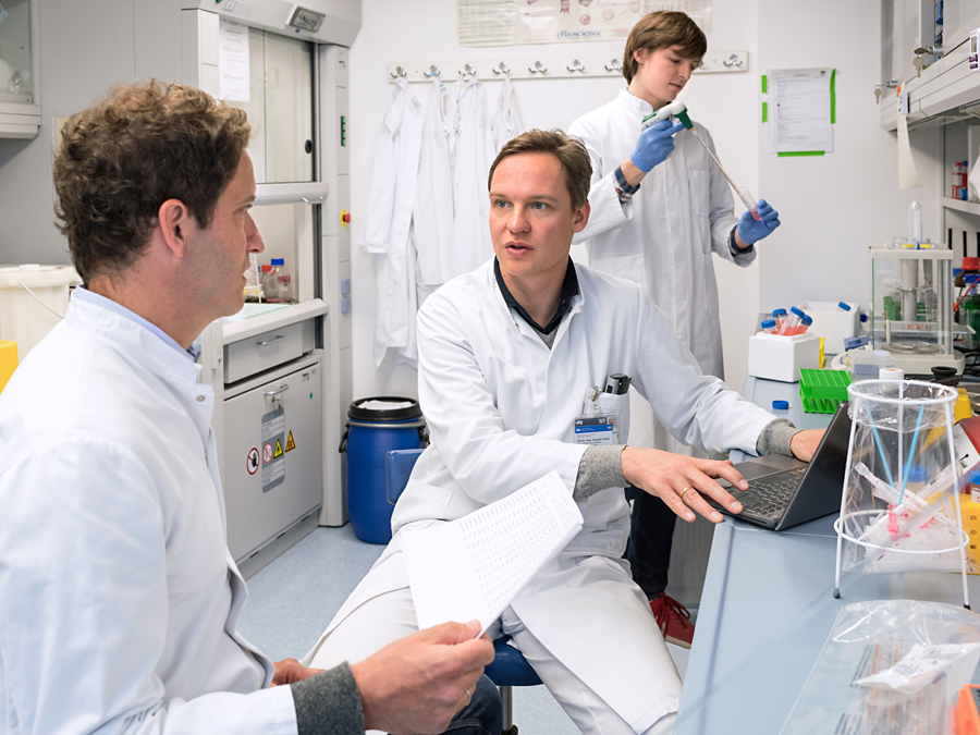 An international team led by PD Dr. Hendrik Poeck (center) and Dr. Tobias Haas (left) has developed a new approach to protect stem cell recipients from graft-versus-host disease. First author Julius Fischer is seen in the right half of the picture. (image The authors of the study talking in a lab room.