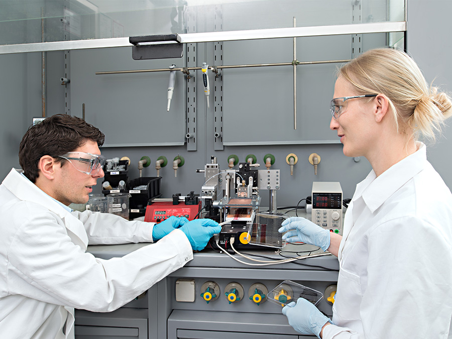 Stephan Pröller (li.) und Dr. Eva M. Herzig vor dem Drucker, mit dem Kunststoff-Solarzellen hergestellt werden.