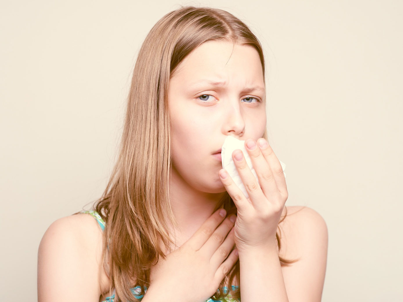 A sick teen girl is coughing in a tissue.