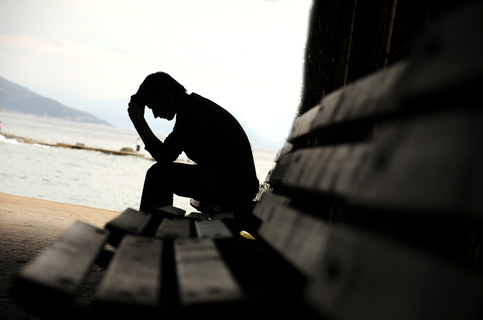 A man sitting on bench holding his head.