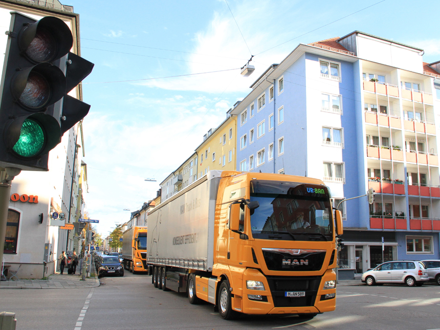 Ein Lkw der Firma MAN fährt durch die Stadt. Im Vordergrund zeigt eine Ampel grün.