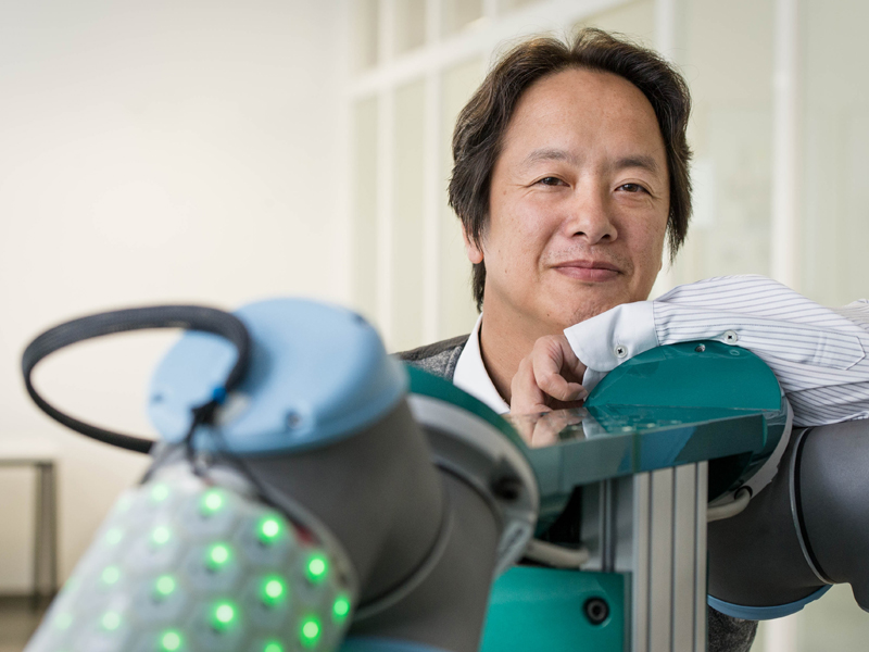 TUM-Prof. Gordon Cheng neben einer seiner Robotik-Kreationen: Ein Roboterarm mit der von Cheng entwickelten künstlichen Haut.