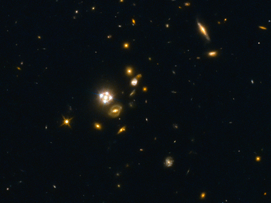 HE0435-1223, in der Mitte des Bildes, gehört zu den fünf besten Gravitationslinsen-Quasaren, die bisher entdeckt wurden. Die Vordergrundgalaxie erzeugt hier vier nahezu gleichmäßig verteilte Bilder des dahinter liegenden Quasars. Bild: Suyu et al. / ESA/Hubble, NASA