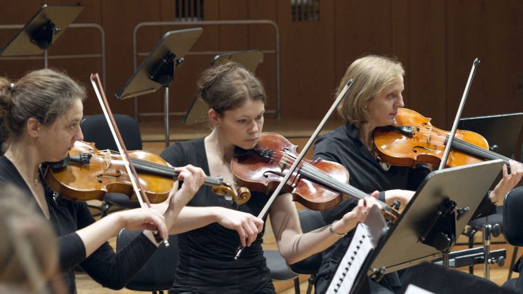 Three violin players of the Symphonic Ensemble during a concert. Three violin players of the Symphonic Ensemble during a concert.